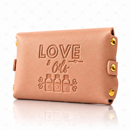 Rosa LOVE & OILS-etui med preget tekst, dekorative flaskemotiver og gullfargede detaljer på lukningen.